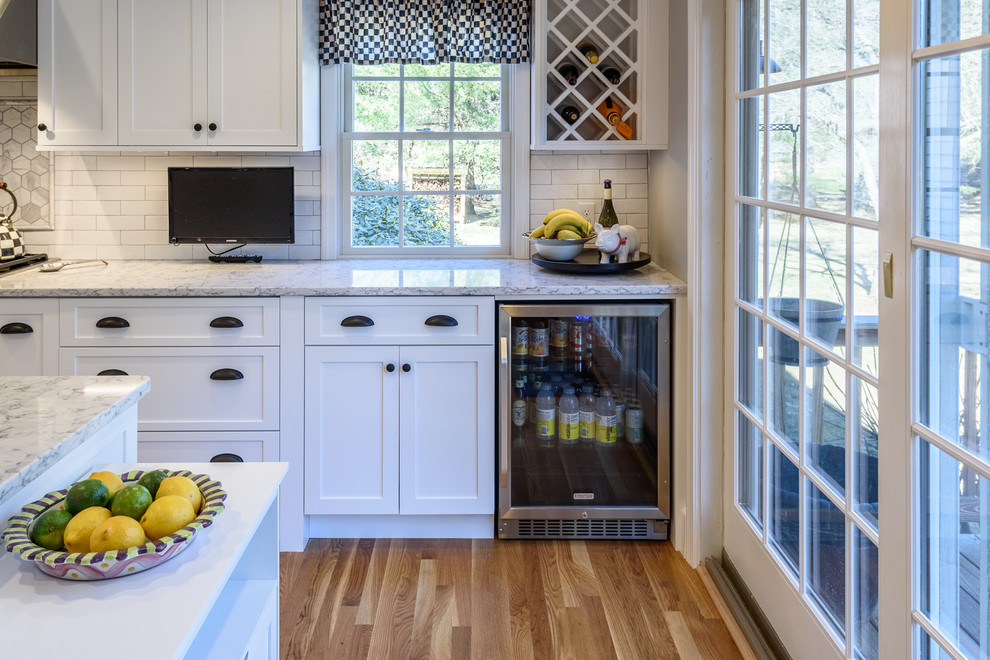 This is an example of a large transitional eat-in kitchen in Boston with a farmhouse sink, shaker cabinets, white cabinets, quartz benchtops, white splashback, stainless steel appliances, medium hardwood floors, porcelain splashback and with island.
