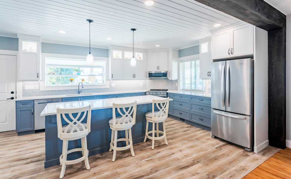 Inspiration for a transitional l-shaped kitchen in Vancouver with an undermount sink, shaker cabinets, blue cabinets, grey splashback, subway tile splashback, stainless steel appliances, with island, beige floor and white benchtop.