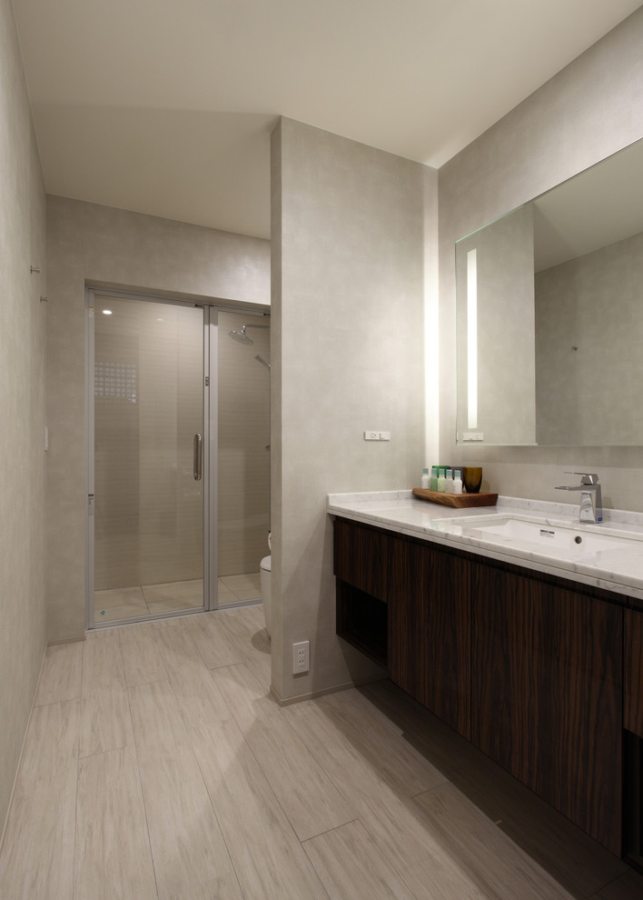 Design ideas for a mid-sized modern powder room in Other with flat-panel cabinets, brown cabinets, a one-piece toilet, beige tile, beige walls, ceramic floors, an undermount sink, solid surface benchtops, beige floor and white benchtops.