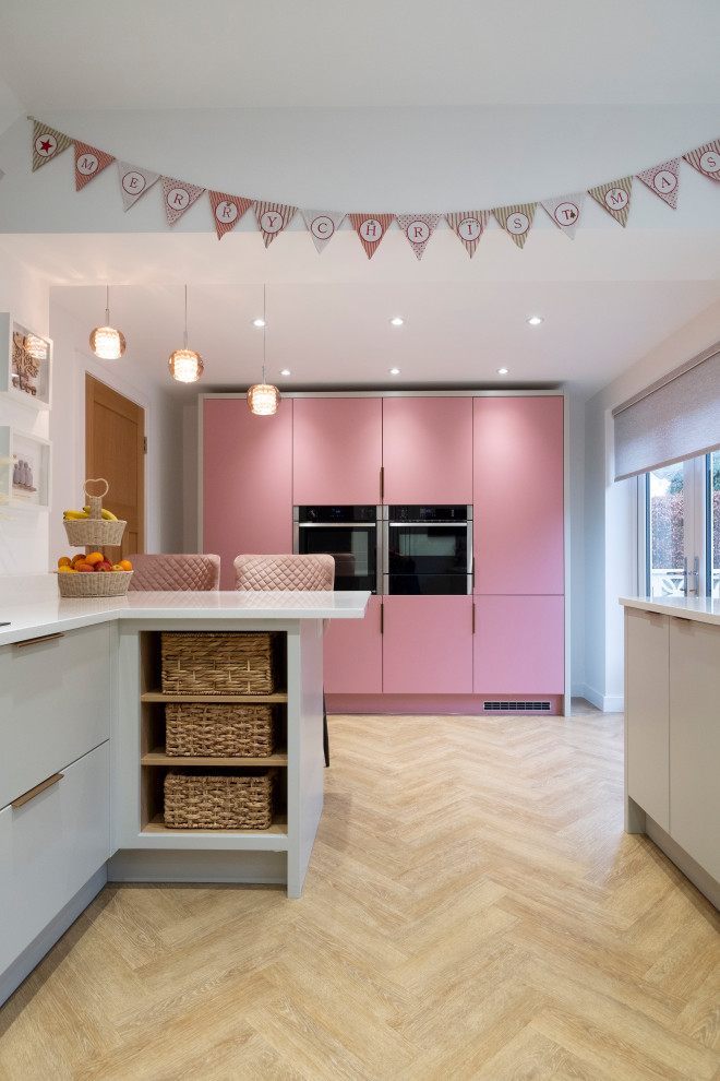 Example of a mid-sized trendy u-shaped laminate floor eat-in kitchen design in Cardiff with an integrated sink, flat-panel cabinets, pink cabinets, quartzite countertops, pink backsplash, glass sheet backsplash, stainless steel appliances, a peninsula and white countertops