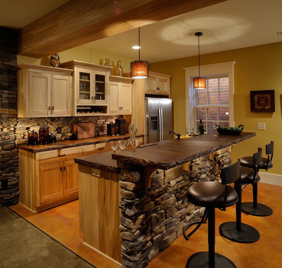 This is an example of a country galley kitchen in Columbus with stainless steel appliances, concrete benchtops, shaker cabinets, light wood cabinets, carpet, with island and exposed beam.