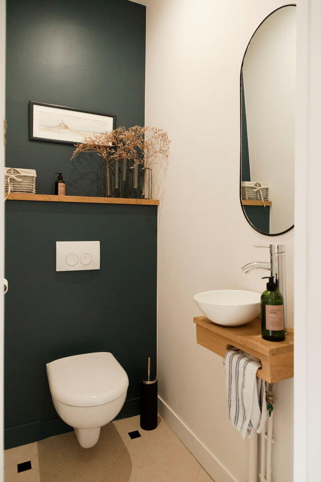 Small powder room in Paris with open cabinets, light wood cabinets, a wall-mount toilet, white walls, porcelain floors, a wall-mount sink, wood benchtops, beige floor and beige benchtops.