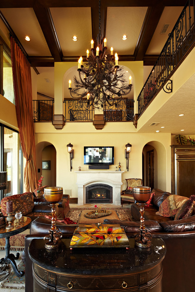This is an example of an expansive mediterranean formal open concept living room in New Orleans with yellow walls, medium hardwood floors, a standard fireplace, a stone fireplace surround and a wall-mounted tv.