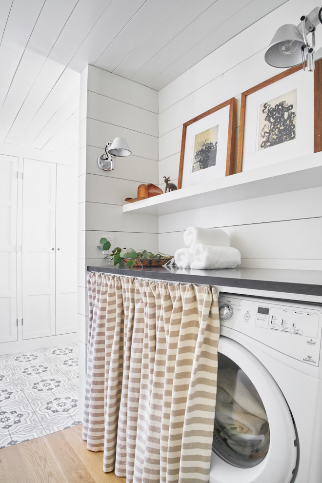 Photo of a mid-sized country single-wall dedicated laundry room in Austin with white cabinets, white walls, light hardwood floors and beige floor.