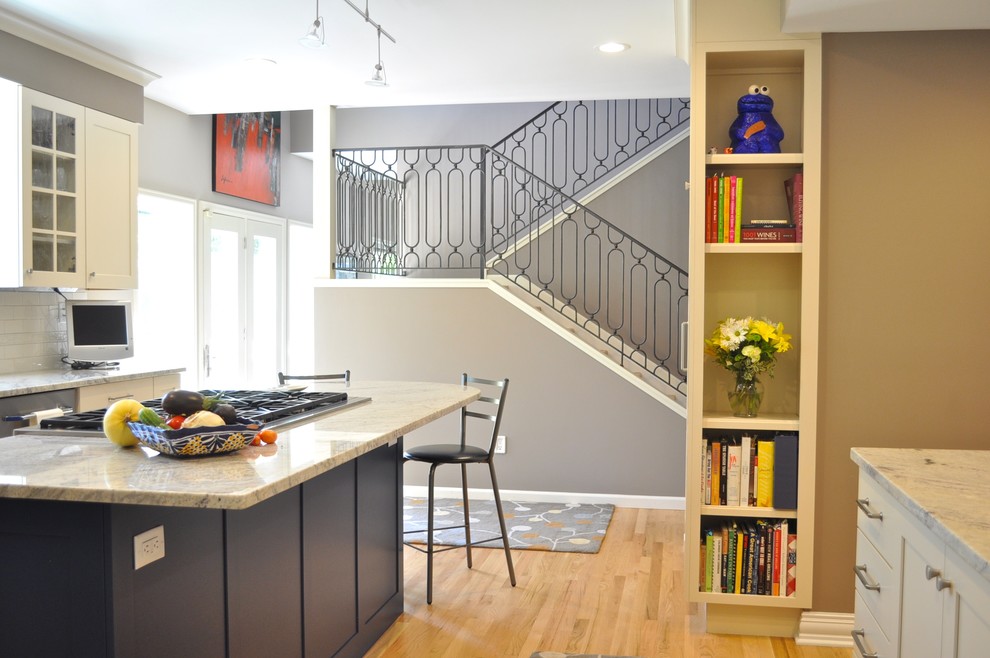 Mid-sized transitional l-shaped light wood floor and brown floor enclosed kitchen photo in Denver with a farmhouse sink, shaker cabinets, white backsplash, ceramic backsplash, an island, white cabinets, marble countertops and stainless steel appliances