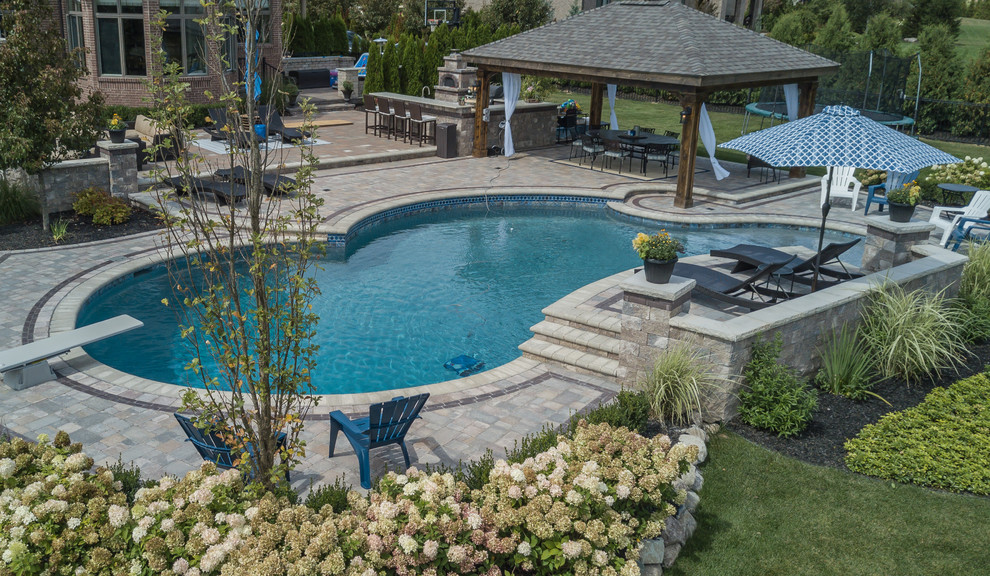 Large transitional backyard custom-shaped pool in Detroit with a water feature and brick pavers.