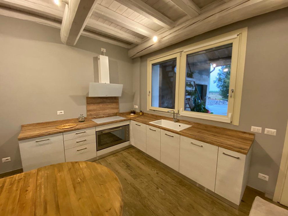 Photo of a mid-sized scandinavian l-shaped eat-in kitchen in Other with a drop-in sink, light wood cabinets, laminate benchtops, stainless steel appliances, light hardwood floors, no island and exposed beam.