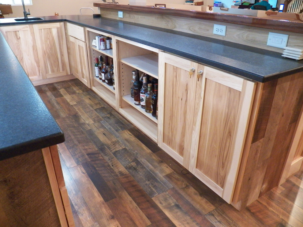 Photo of a large country u-shaped wet bar in Cincinnati with an undermount sink, shaker cabinets, light wood cabinets, granite benchtops, laminate floors, brown floor and black benchtop.