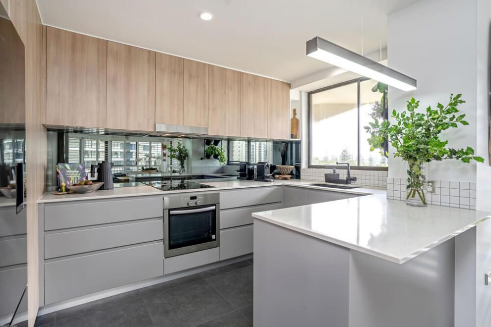 Inspiration for a mid-sized contemporary u-shaped kitchen in Gold Coast - Tweed with an undermount sink, flat-panel cabinets, white splashback, glass sheet splashback, porcelain floors, a peninsula, grey floor and white benchtop.