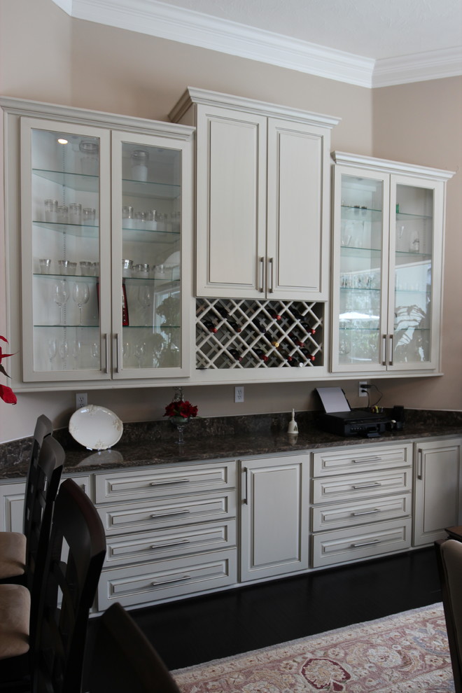 Photo of a mid-sized traditional single-wall wet bar in Jacksonville with raised-panel cabinets, white cabinets, quartzite benchtops, dark hardwood floors, brown floor, no sink and black benchtop.