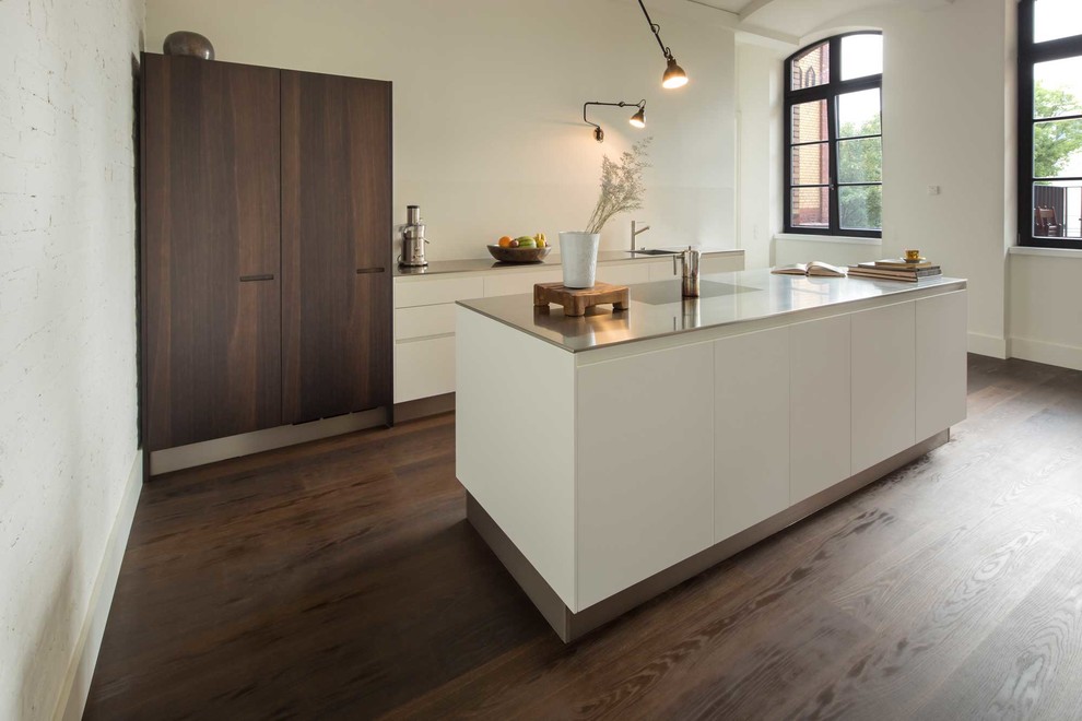 This is an example of a mid-sized contemporary open plan kitchen in Berlin with raised-panel cabinets, white cabinets, stainless steel benchtops, white splashback, a single-bowl sink, panelled appliances, with island and dark hardwood floors.
