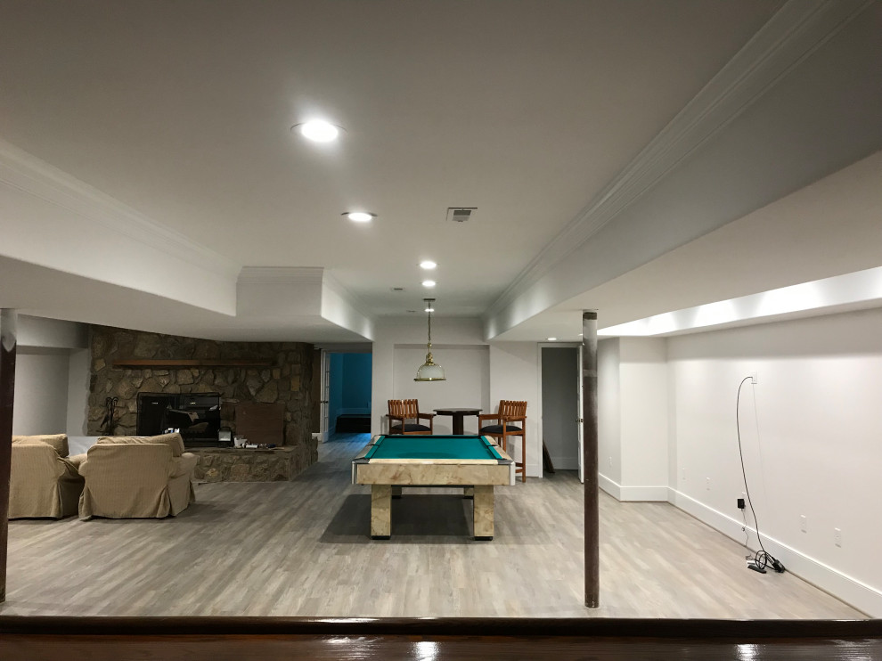 Example of a large trendy underground laminate floor and gray floor basement design in Other with white walls, a standard fireplace and a stone fireplace
