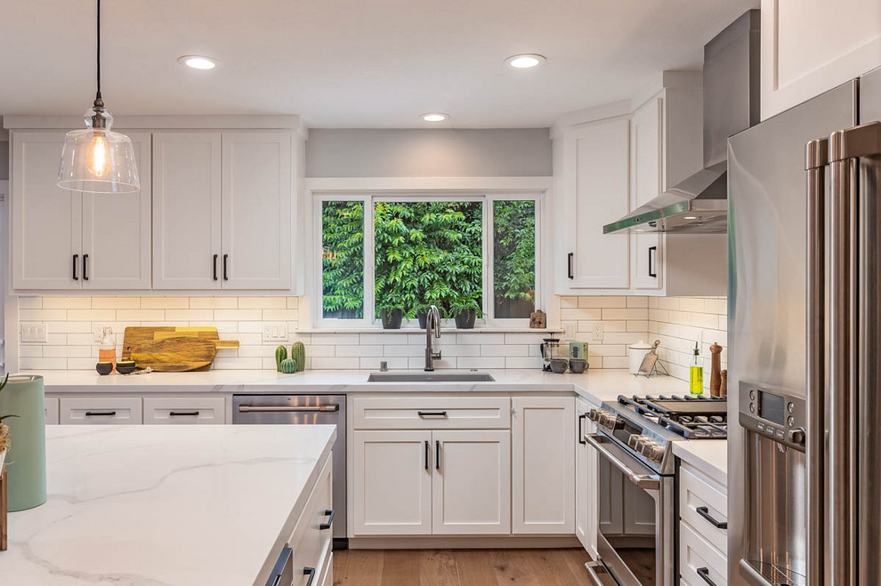 Inspiration for a mid-sized transitional u-shaped eat-in kitchen in San Francisco with an undermount sink, shaker cabinets, white cabinets, quartz benchtops, white splashback, subway tile splashback, stainless steel appliances, light hardwood floors, with island, beige floor and white benchtop.