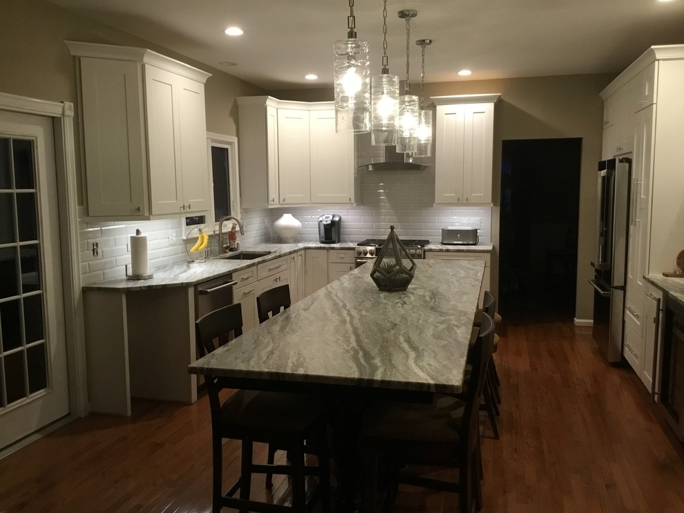 Inspiration for a mid-sized transitional u-shaped medium tone wood floor and brown floor open concept kitchen remodel in DC Metro with an undermount sink, white cabinets, granite countertops, white backsplash, subway tile backsplash, stainless steel appliances, an island, gray countertops and shaker cabinets
