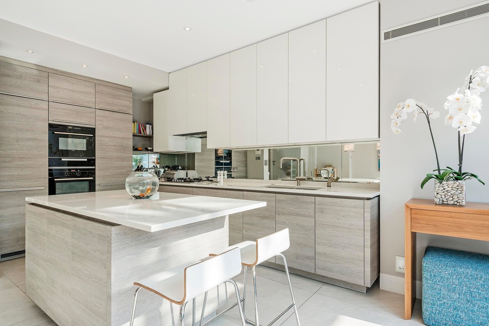 Photo of a mid-sized modern l-shaped kitchen in London with an undermount sink, flat-panel cabinets, grey cabinets, metallic splashback, mirror splashback, panelled appliances, with island and grey floor.