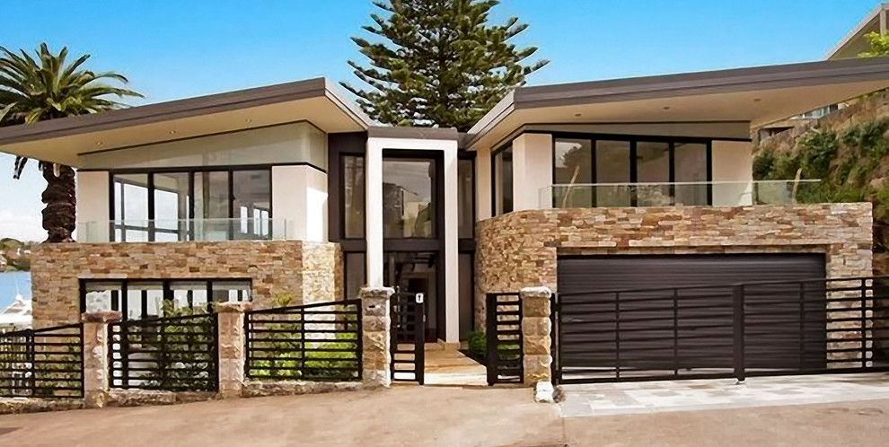 Photo of a large contemporary two-storey beige house exterior in Sydney with stone veneer and a flat roof.