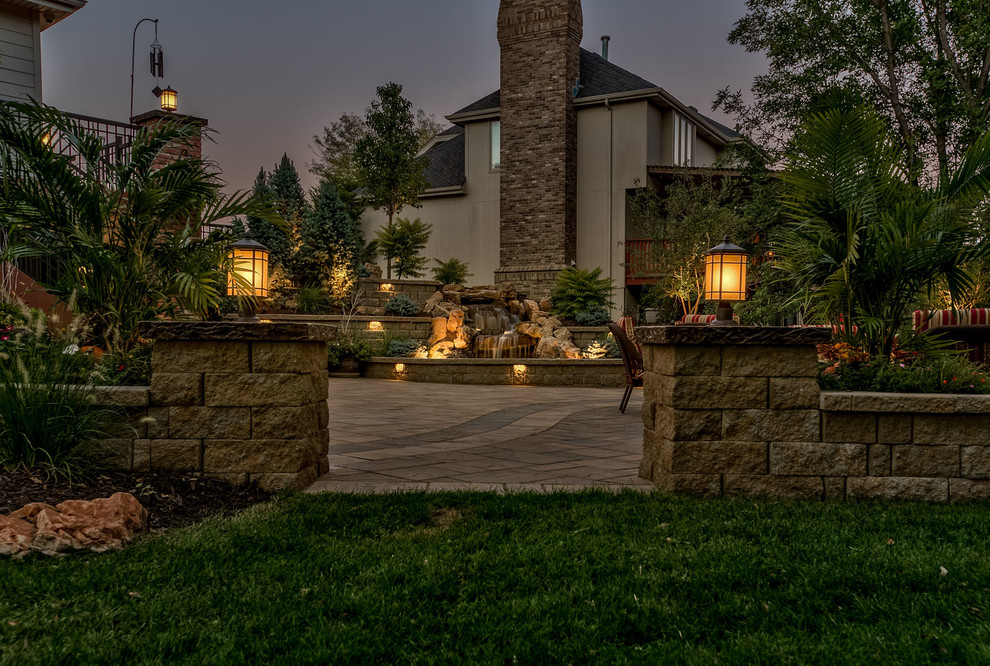 This is an example of a large traditional backyard patio in Omaha with a water feature and concrete pavers.