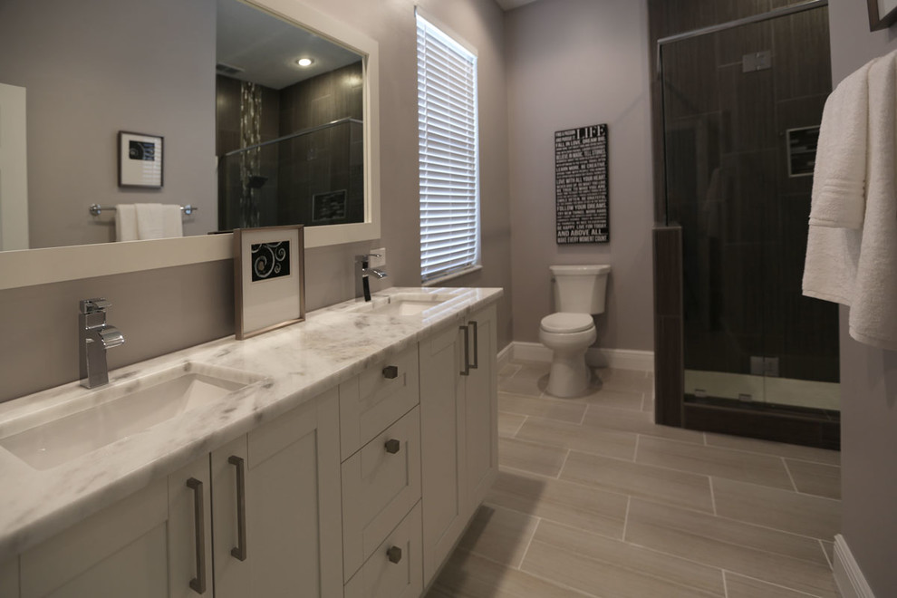 Photo of a large transitional master bathroom in Tampa with recessed-panel cabinets, white cabinets, an alcove shower, a one-piece toilet, grey walls, laminate floors, an undermount sink, beige floor and a hinged shower door.