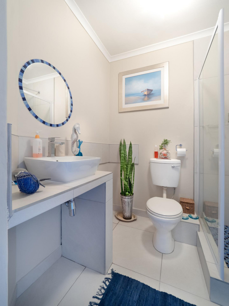 Maritim inredning av ett litet vit vitt en-suite badrum, med vita skåp, en hörndusch, en toalettstol med hel cisternkåpa, vit kakel, vita väggar, klinkergolv i porslin, bänkskiva i kvarts, vitt golv och dusch med skjutdörr