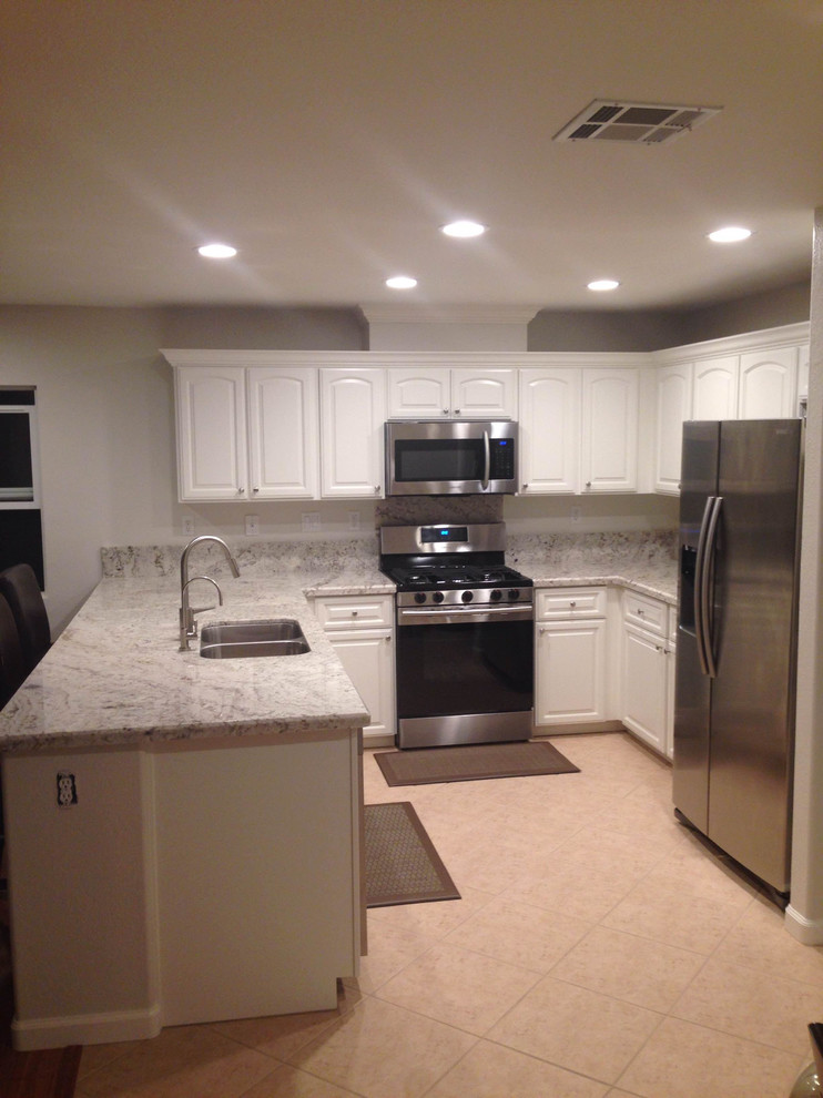 Mid-sized elegant u-shaped porcelain tile and white floor enclosed kitchen photo in San Diego with a double-bowl sink, raised-panel cabinets, white cabinets, granite countertops, gray backsplash, stone slab backsplash, stainless steel appliances and a peninsula