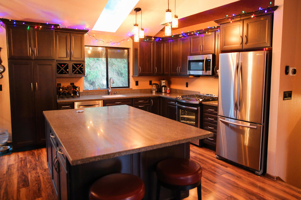 Example of a mid-sized transitional l-shaped medium tone wood floor open concept kitchen design in Seattle with an integrated sink, flat-panel cabinets, dark wood cabinets, solid surface countertops, stainless steel appliances and an island