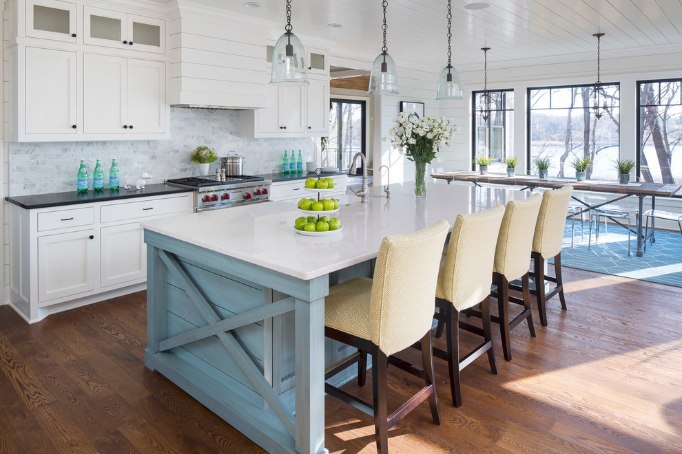 Inspiration for a single-wall medium tone wood floor open concept kitchen remodel in Minneapolis with a farmhouse sink, shaker cabinets, white cabinets, marble countertops, marble backsplash, stainless steel appliances and an island