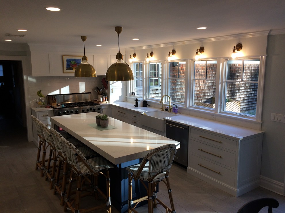 This is an example of a mid-sized transitional l-shaped eat-in kitchen in New York with a farmhouse sink, shaker cabinets, white cabinets, quartz benchtops, white splashback, subway tile splashback, stainless steel appliances, porcelain floors, with island and grey floor.