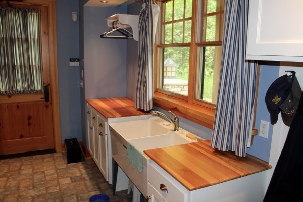This is an example of a mid-sized country single-wall dedicated laundry room in Milwaukee with a farmhouse sink, recessed-panel cabinets, white cabinets, wood benchtops and blue walls.