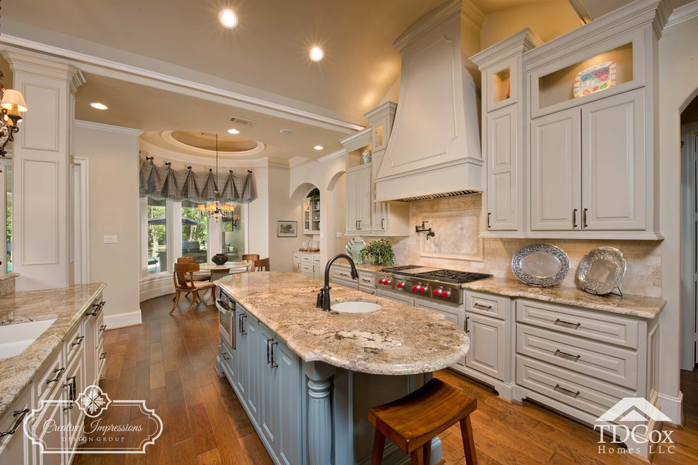 Large transitional u-shaped medium tone wood floor and beige floor open concept kitchen photo in Houston with an undermount sink, shaker cabinets, white cabinets, granite countertops, beige backsplash, travertine backsplash, black appliances and an island