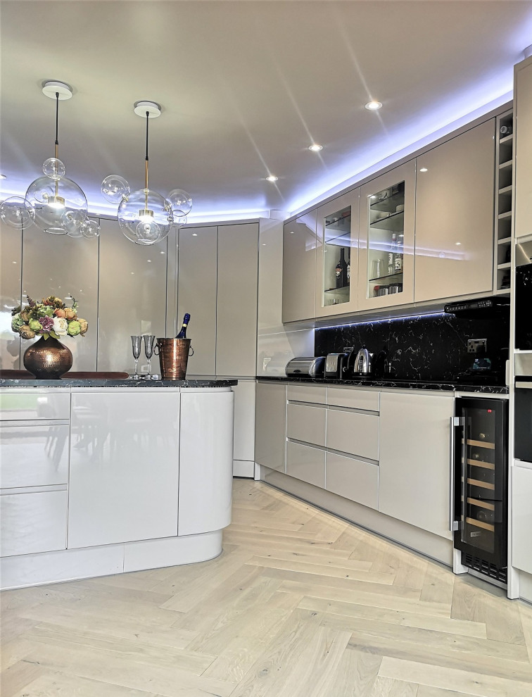 Photo of a large contemporary cream and black open plan kitchen in London with flat-panel cabinets, beige cabinets, quartz worktops, multi-coloured splashback, engineered quartz splashback, black appliances, light hardwood flooring, an island, beige floors, multicoloured worktops and a drop ceiling.