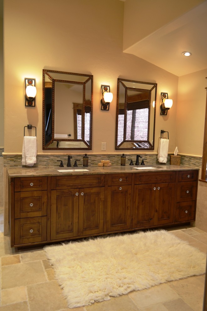 Mid-sized mountain style master travertine floor and beige floor bathroom photo with an undermount sink, recessed-panel cabinets, brown cabinets, beige walls and granite countertops