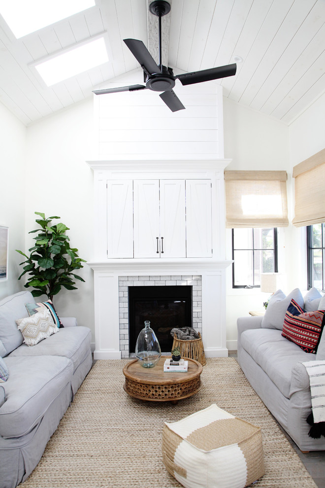 Inspiration for a beach style formal open concept living room in Los Angeles with white walls, a standard fireplace, a concealed tv and grey floor.