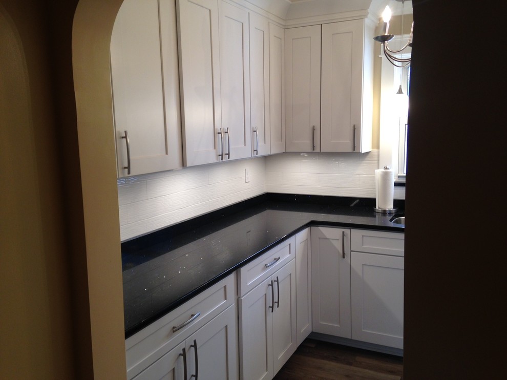 Mid-sized arts and crafts u-shaped vinyl floor home design photo with a double-bowl sink, shaker cabinets, white cabinets, quartz countertops, white backsplash, porcelain backsplash, stainless steel appliances and no island