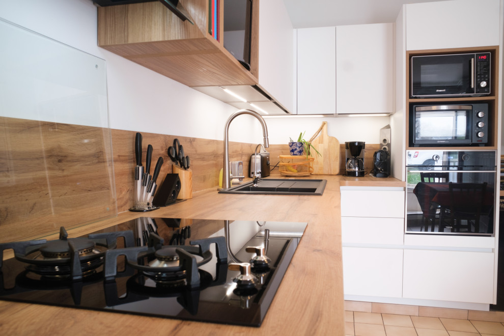 This is an example of a modern l-shaped open plan kitchen in Paris with an integrated sink, wood benchtops, beige splashback, timber splashback, black appliances and beige benchtop.