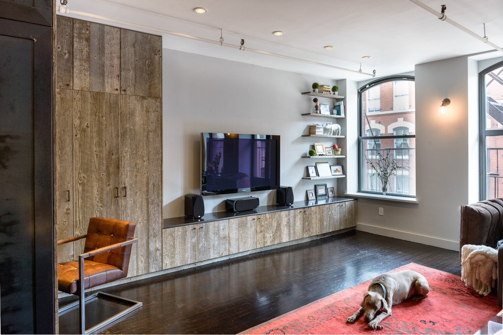 Photo of a mid-sized industrial formal living room in New York with grey walls, dark hardwood floors, no fireplace, a wall-mounted tv and brown floor.