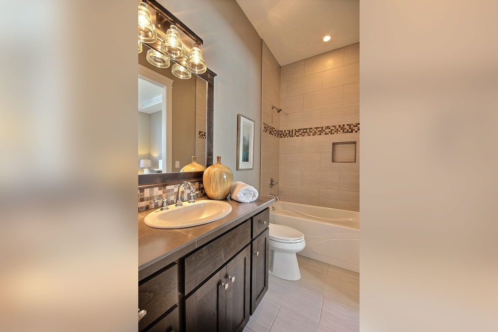Photo of a mid-sized transitional master bathroom in Portland with recessed-panel cabinets, dark wood cabinets, an alcove tub, a shower/bathtub combo, a two-piece toilet, brown tile, porcelain tile, beige walls, porcelain floors, a drop-in sink and tile benchtops.