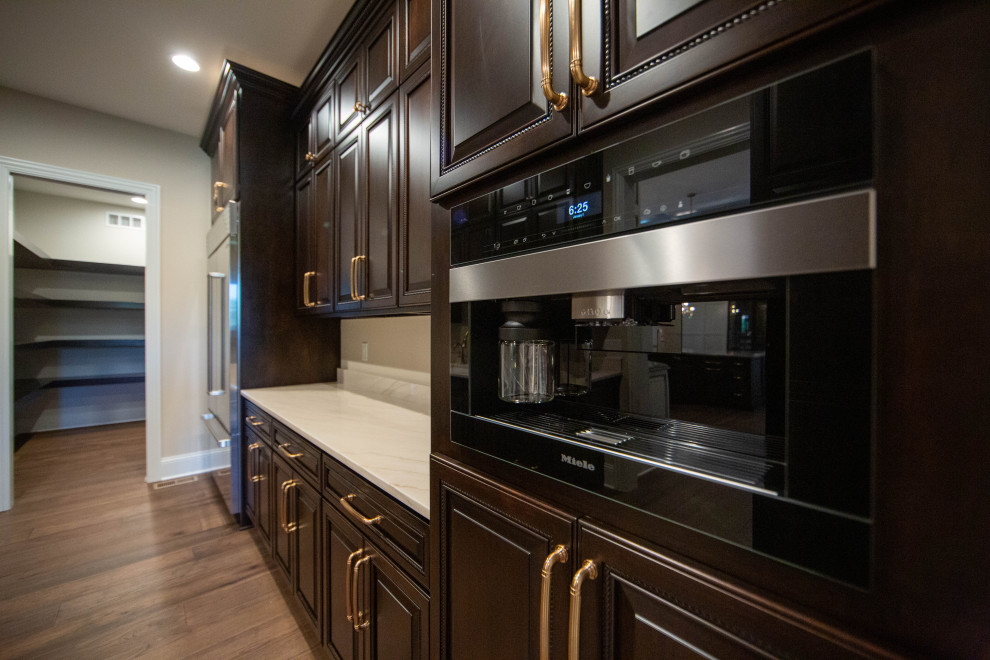 Photo of a large transitional galley kitchen pantry in Indianapolis with raised-panel cabinets, dark wood cabinets, granite benchtops, stainless steel appliances, laminate floors, brown floor and white benchtop.