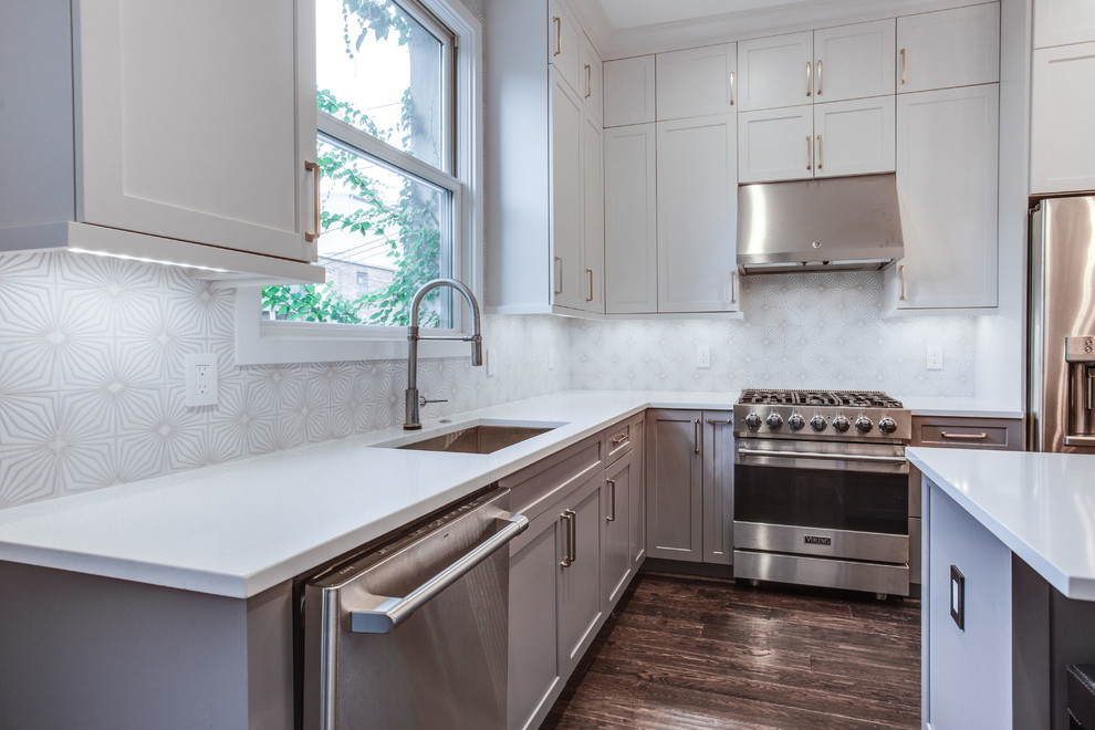 Inspiration for a large transitional l-shaped medium tone wood floor and brown floor eat-in kitchen remodel in DC Metro with an undermount sink, shaker cabinets, white cabinets, solid surface countertops, white backsplash, ceramic backsplash, stainless steel appliances, an island and white countertops