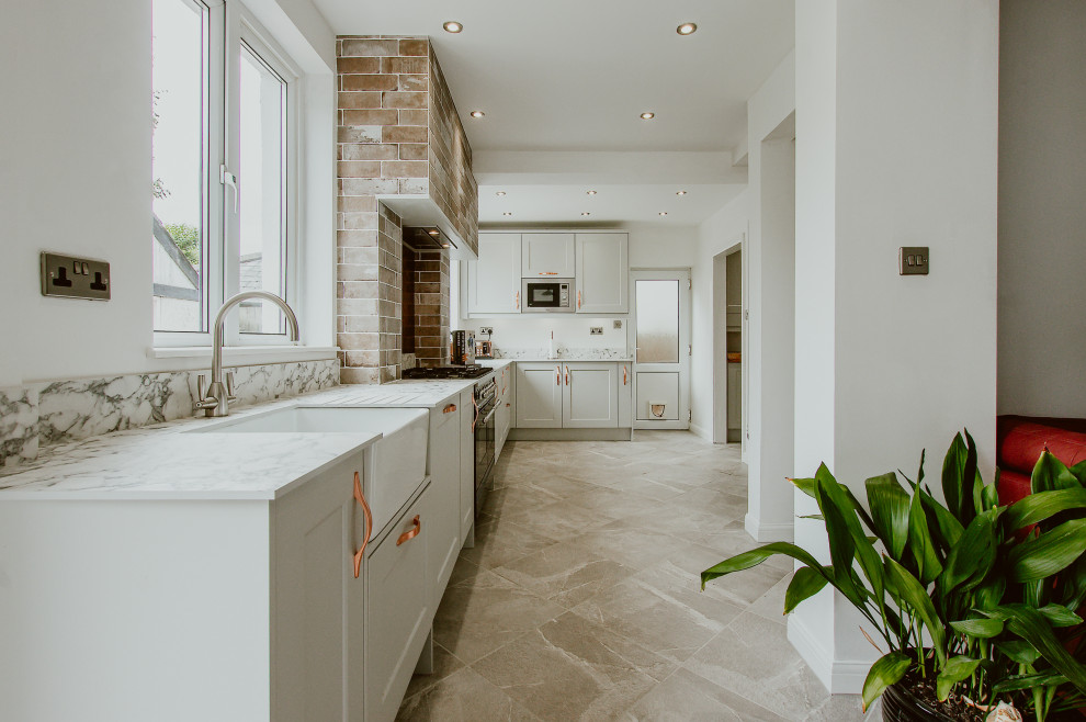Example of a mid-sized classic l-shaped porcelain tile and gray floor enclosed kitchen design in Cardiff with a farmhouse sink, shaker cabinets, gray cabinets, marble countertops, metallic backsplash, metal backsplash, stainless steel appliances, no island and white countertops