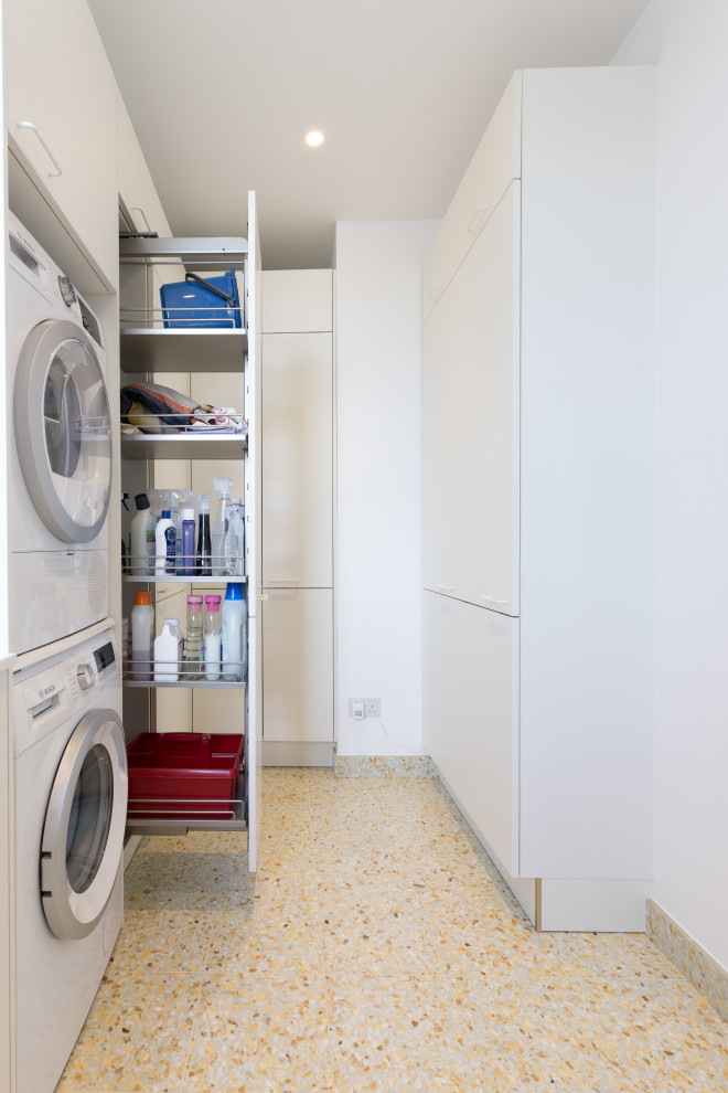 Large contemporary l-shaped dedicated laundry room in London with a drop-in sink, flat-panel cabinets, white cabinets, solid surface benchtops, white splashback, ceramic splashback, white walls, porcelain floors, a stacked washer and dryer, green floor and white benchtop.