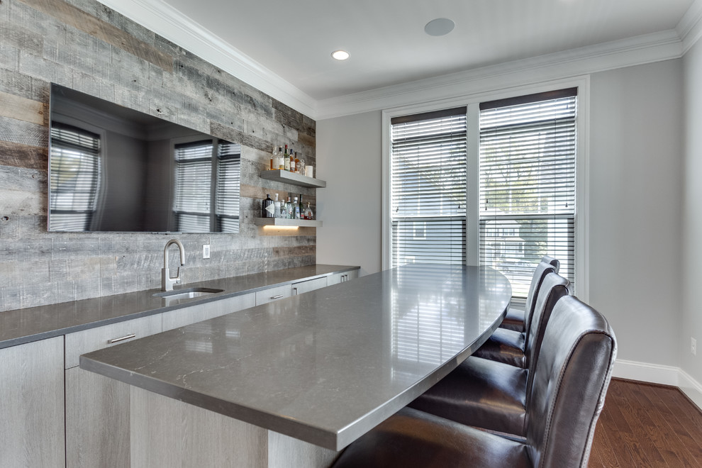This is an example of a mid-sized modern galley seated home bar in DC Metro with an undermount sink, quartz benchtops, grey splashback and medium hardwood floors.
