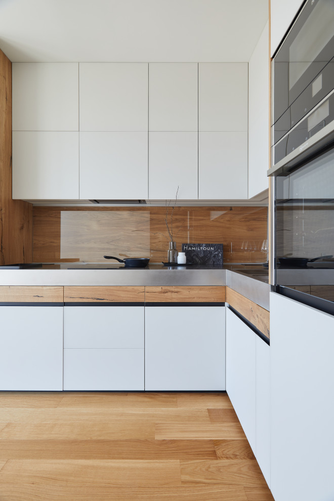 Inspiration for a mid-sized l-shaped eat-in kitchen in Moscow with a double-bowl sink, white cabinets, stainless steel benchtops, brown splashback, timber splashback, panelled appliances, no island and grey benchtop.