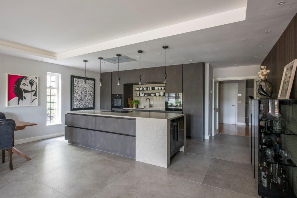 This is an example of a large contemporary grey and brown galley open plan kitchen in Manchester with a submerged sink, flat-panel cabinets, grey cabinets, quartz worktops, beige splashback, stone slab splashback, black appliances, porcelain flooring, an island, grey floors, beige worktops, a coffered ceiling and a feature wall.