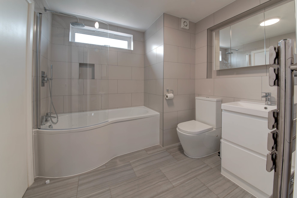Inspiration for a large contemporary kids bathroom in Surrey with flat-panel cabinets, white cabinets, a drop-in tub, a shower/bathtub combo, a two-piece toilet, beige tile, ceramic tile, beige walls, porcelain floors, a drop-in sink, multi-coloured floor and a hinged shower door.