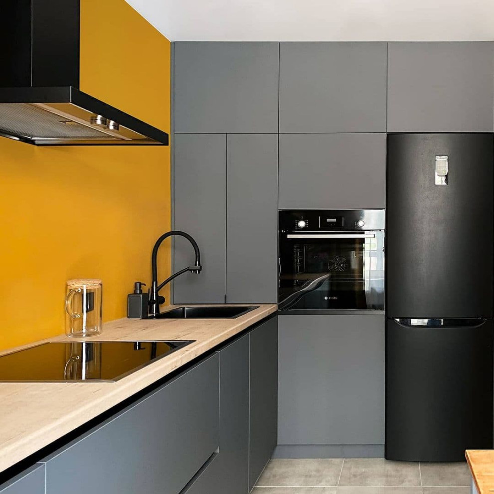 Mid-sized contemporary l-shaped eat-in kitchen in Moscow with an undermount sink, flat-panel cabinets, grey cabinets, wood benchtops, orange splashback, limestone splashback, black appliances, ceramic floors, no island, grey floor and brown benchtop.