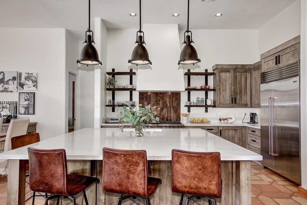 This is an example of a mid-sized industrial l-shaped eat-in kitchen in Phoenix with an undermount sink, shaker cabinets, distressed cabinets, quartz benchtops, brown splashback, porcelain splashback, stainless steel appliances, terra-cotta floors, with island and white benchtop.