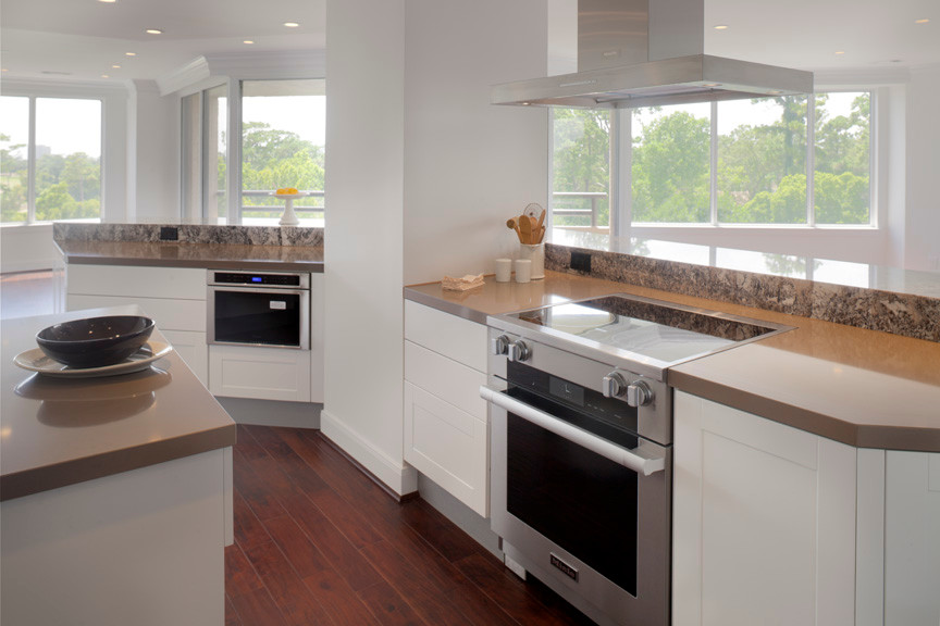 Mid-sized minimalist galley medium tone wood floor eat-in kitchen photo in Houston with an undermount sink, flat-panel cabinets, white cabinets, solid surface countertops, brown backsplash, stone slab backsplash, stainless steel appliances and an island