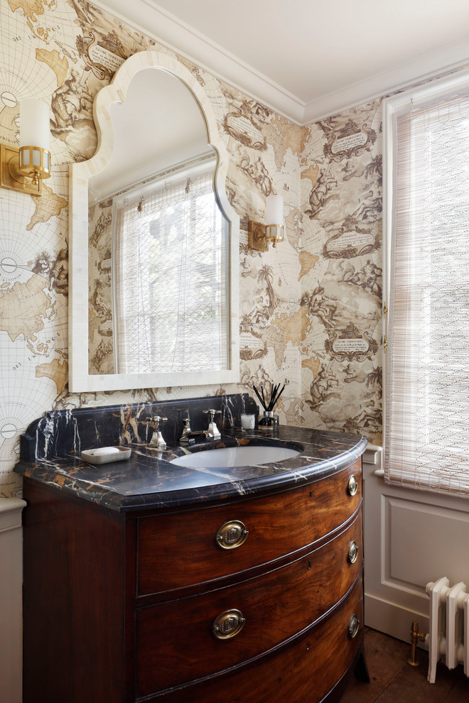 Small transitional powder room in London with furniture-like cabinets, medium wood cabinets, a one-piece toilet, beige tile, beige walls, medium hardwood floors, an undermount sink, marble benchtops, brown floor and black benchtops.
