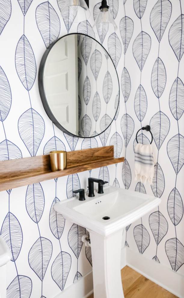 Inspiration for a small beach style powder room in Charleston with a one-piece toilet, blue tile, light hardwood floors, a pedestal sink and wallpaper.