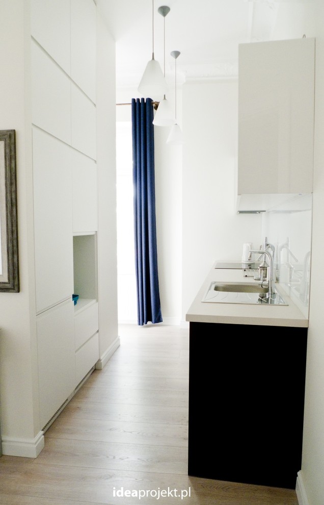 Example of a mid-sized eclectic formal, open concept and galley light wood floor eat-in kitchen design with beige walls, a concealed tv, a single-bowl sink, flat-panel cabinets, brown cabinets, laminate countertops, white backsplash, glass sheet backsplash, stainless steel appliances and no island